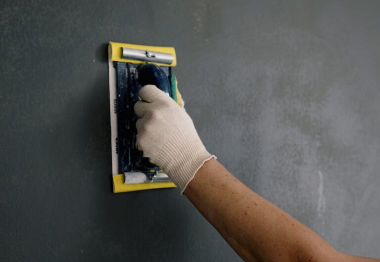Close-up of a hand smoothing a wall with a spackle tool during home renovation