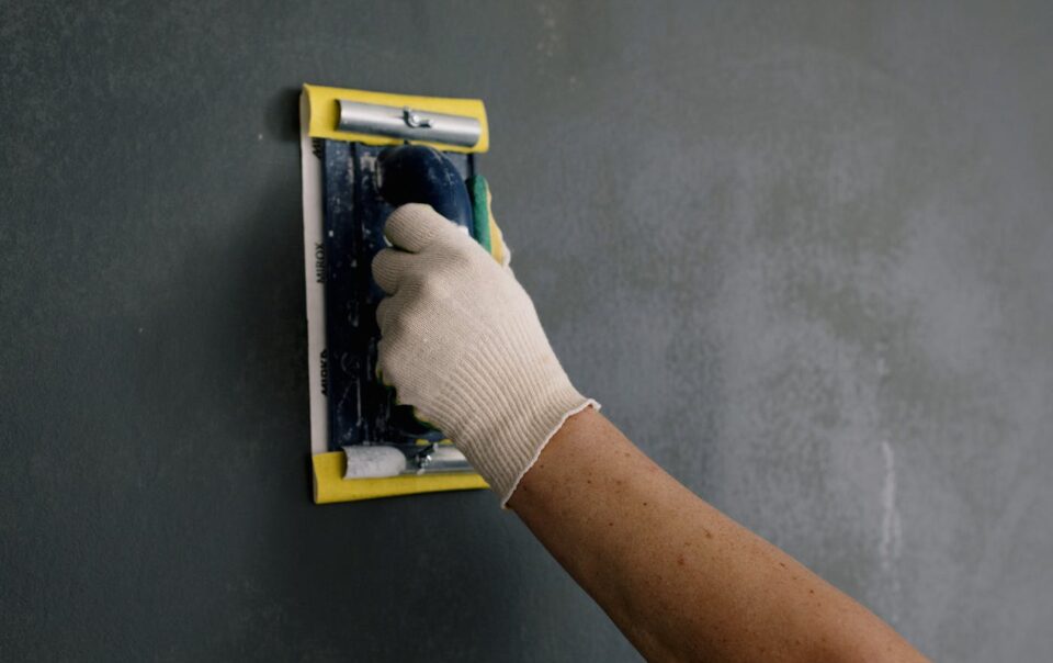 Close-up of a hand smoothing a wall with a spackle tool during home renovation