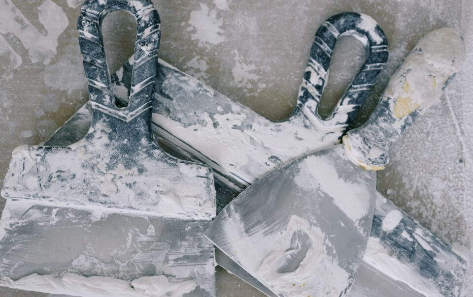 Chaotic arrangement of plastering tools smeared with white plaster, viewed from above.